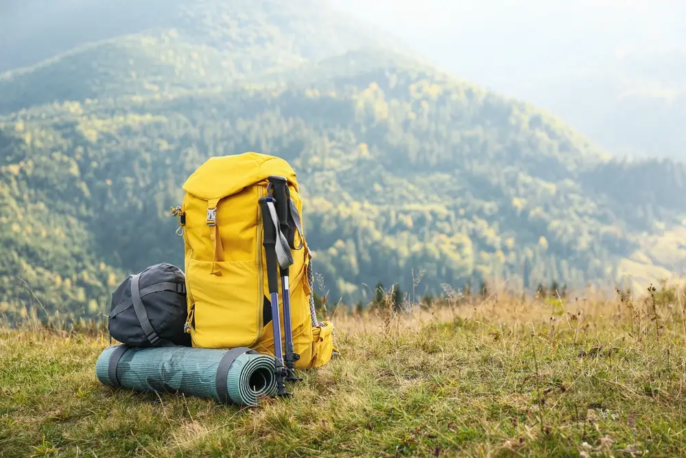 A yellow backpack and hiking gear on a mountain trail, symbolizing adventurous alternatives to Maldives tour packages from Bangladesh
