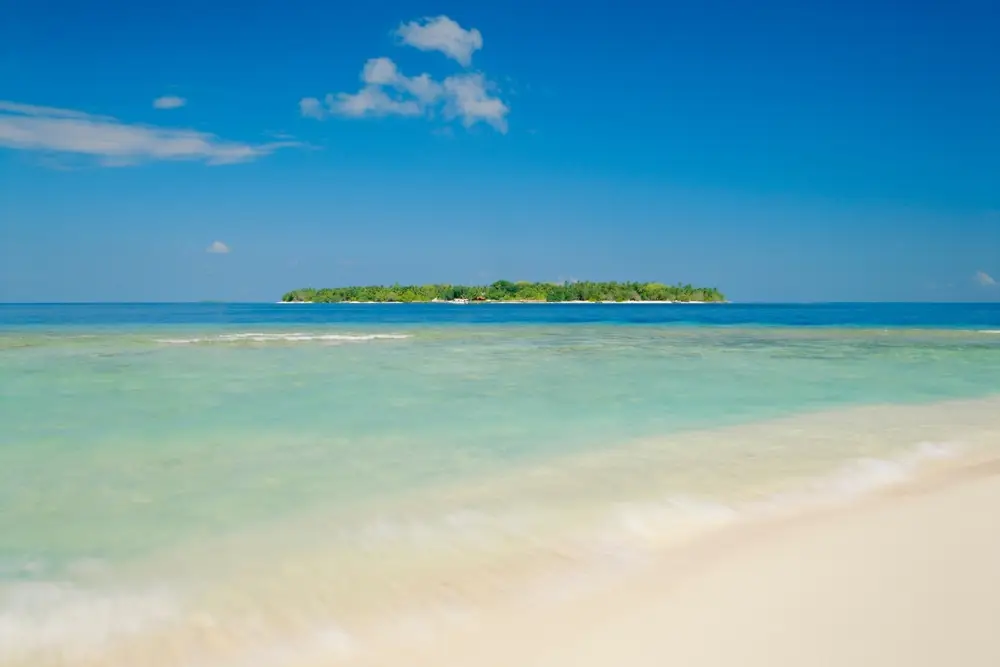 A peaceful view of a remote Maldivian island across crystal-clear waters, often included in Maldives tour packages from Bangladesh for a secluded beach experience