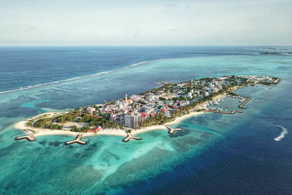 Aerial view of a Maldivian island with clear blue waters and beach resorts, featured in Maldives tour packages from Bangladesh for a serene island escape