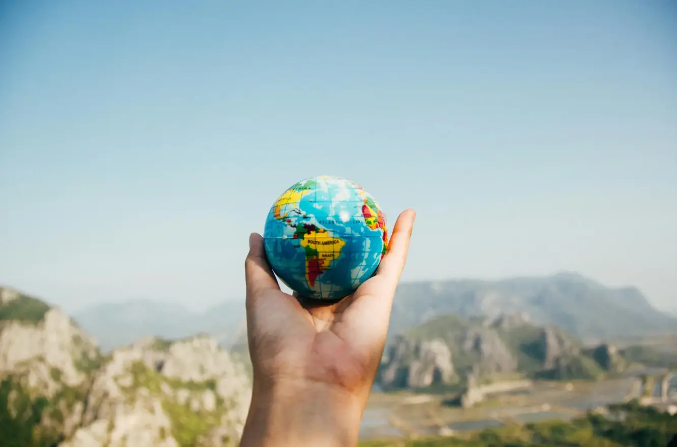 A hand presents a globe showing the Americas before a mountain vista, symbolizing global exploration by your premier Tour and Travel Agency in Bangladesh